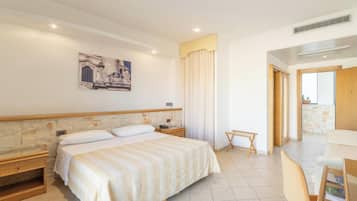 Une chambre d’hôtel avec un grand lit, une tête de lit en bois, une petite table de chevet, une commode, un tableau accroché au mur, une fenêtre avec des rideaux et une vue sur l’extérieur.