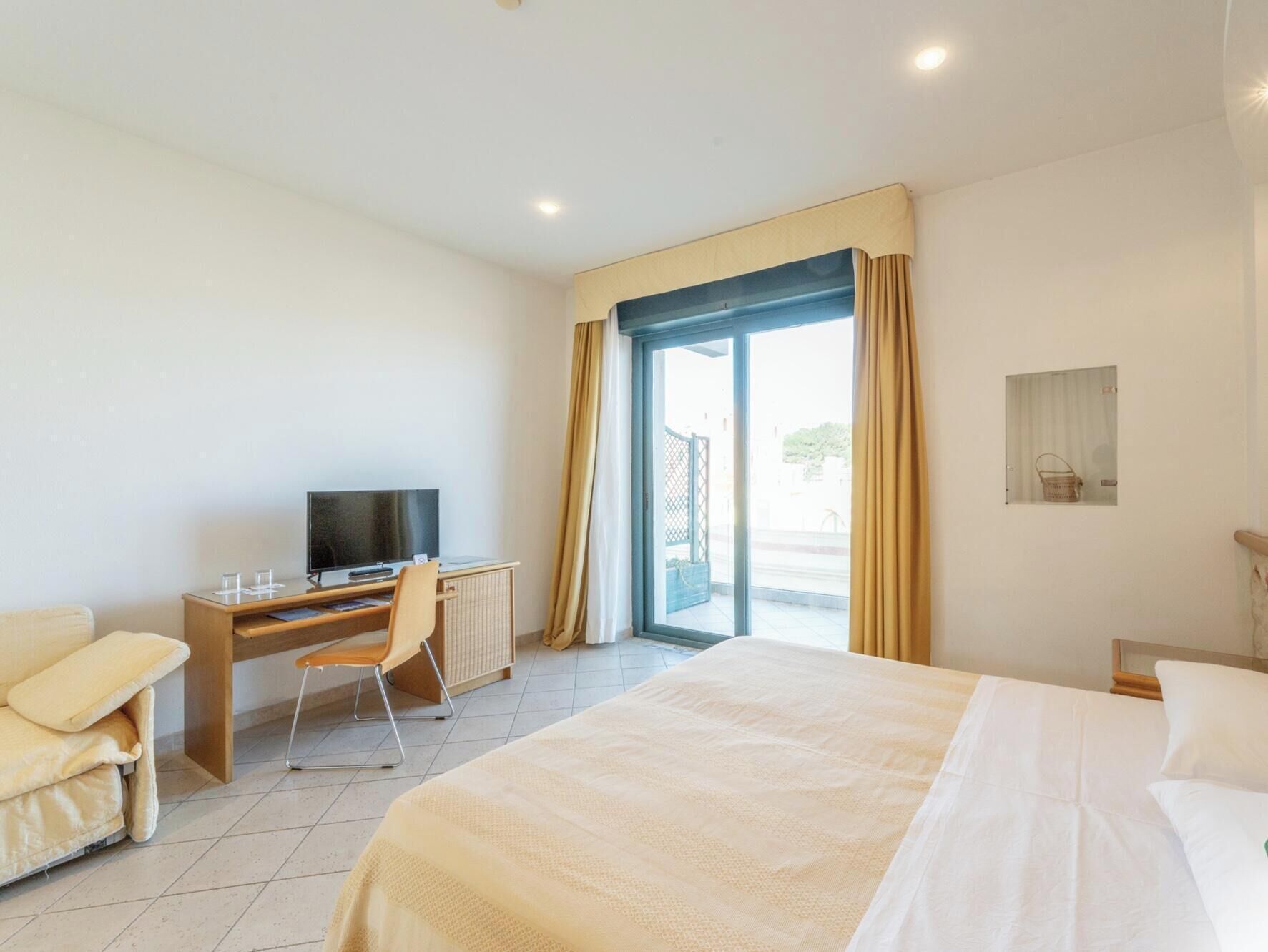 Une chambre d’hôtel avec un lit, un bureau avec une télévision, une chaise et une fenêtre avec des rideaux.