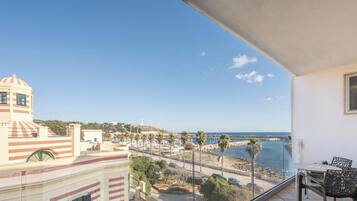 Un balcón con vista a un puerto deportivo, palmeras y un paisaje costero.