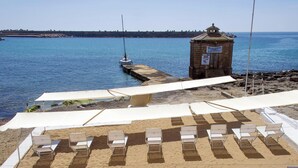 A beachside area with white sun loungers and umbrellas, a small tower structure, and a body of water. - Hotiday Leuca Lungomare (Castrignano del Capo)