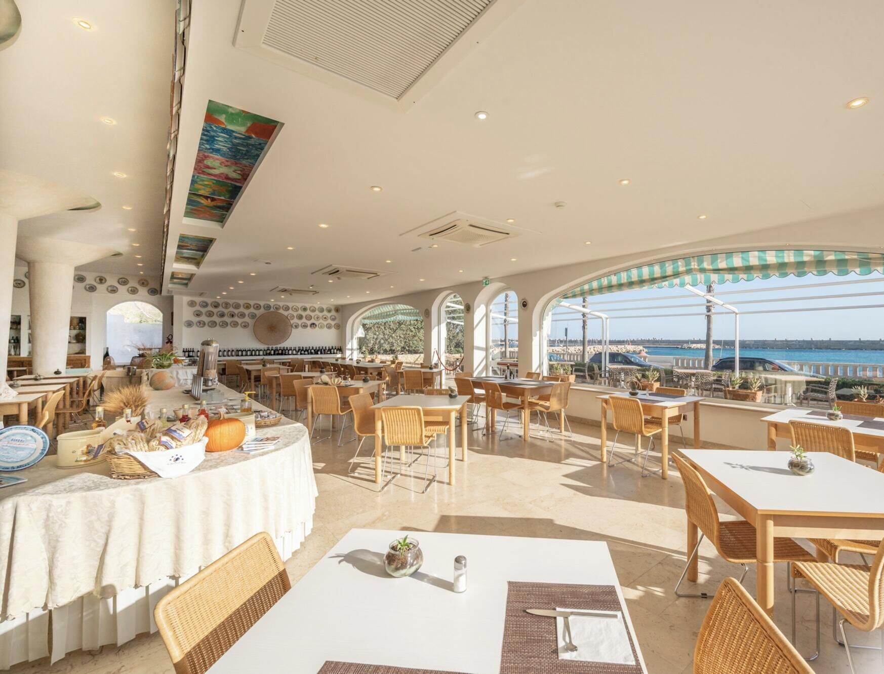 Un restaurante con vistas al mar, que cuenta con mesas y sillas, una zona de bar e iluminación empotrada en el techo.