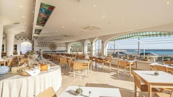 Un restaurante con vistas al mar, que cuenta con mesas y sillas, una zona de bar e iluminación empotrada en el techo.