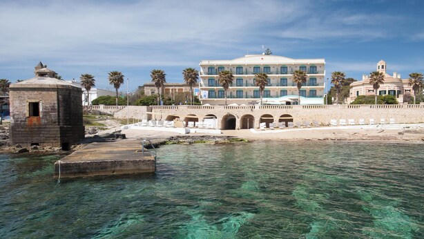 A coastal hotel with clear blue waters, a stone bridge, and palm trees. - Hotiday Leuca Lungomare (Castrignano del Capo)