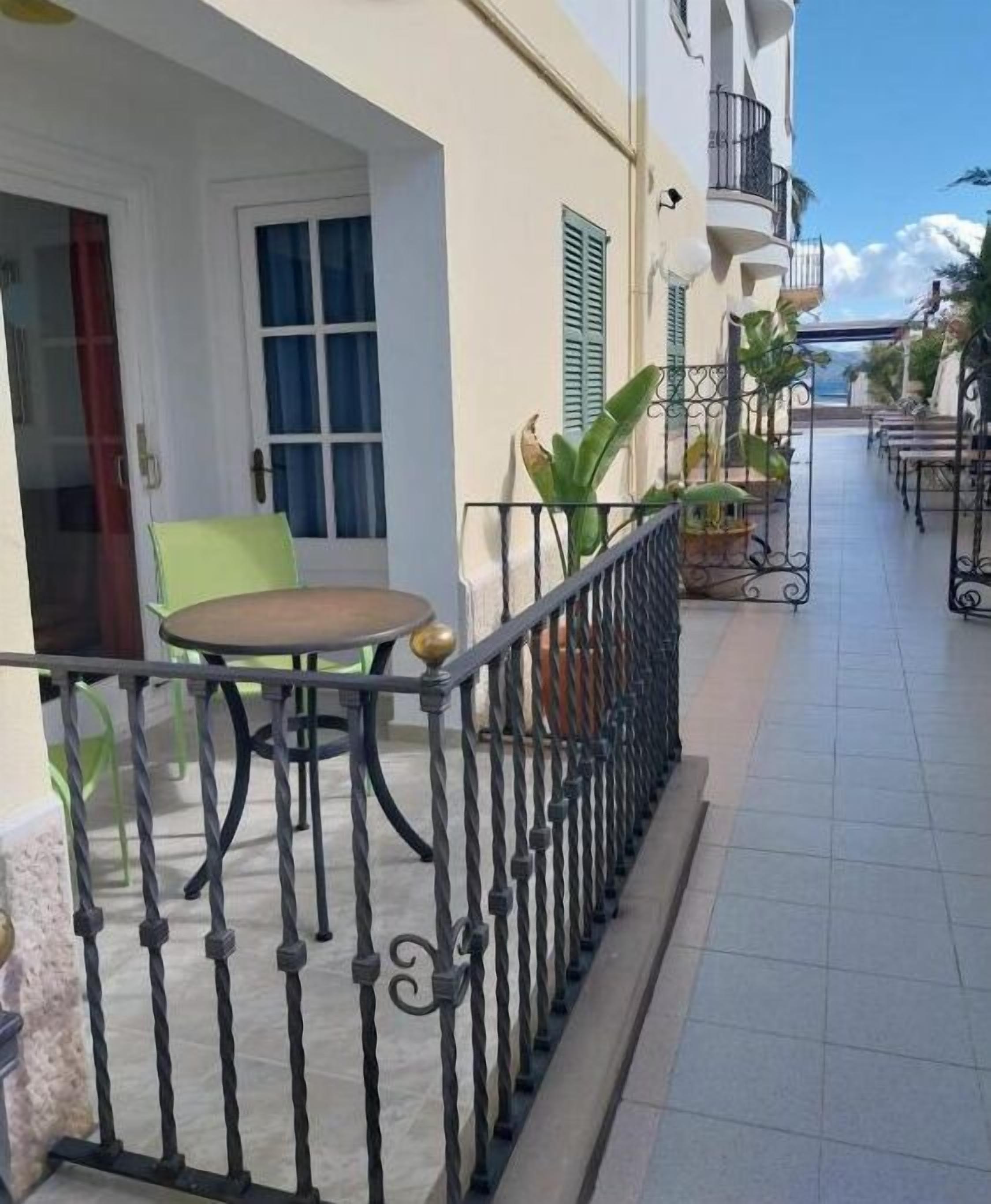 A balcony with a table and chairs, a door, and a window with shutters.