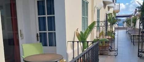 A balcony with a table and chairs, a door, and a window with shutters.