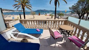 Ein Balkon mit Blick auf Strand und Boote, ausgestattet mit Liegestühlen und einem Tisch.