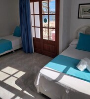 A room with two beds, a wooden door with glass panels, and a view of a beach and palm trees.