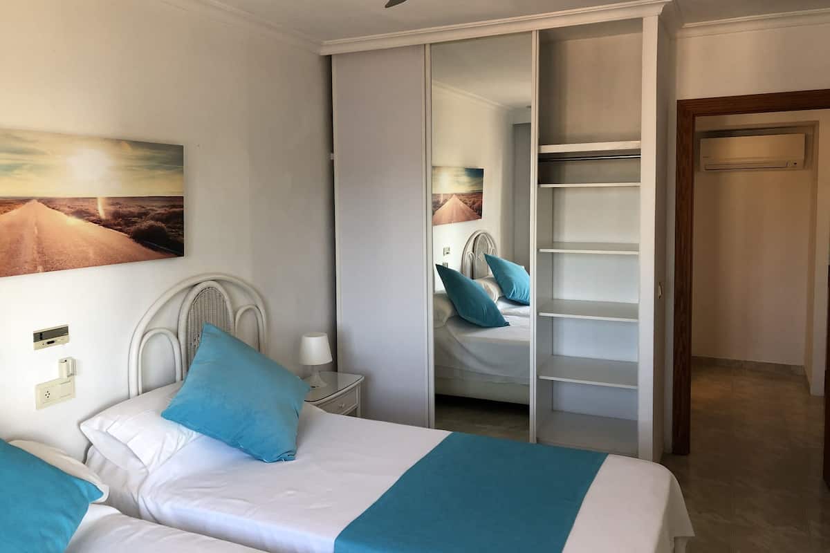 Un dormitorio con cama, mesita de noche, espejo, ventilador de techo y armario.