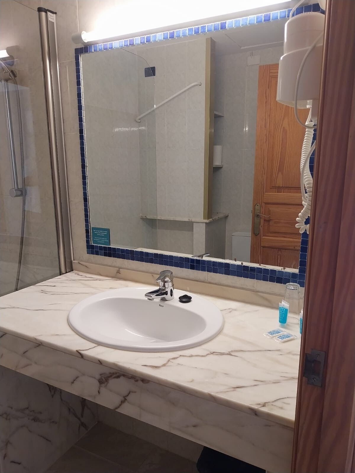 A bathroom with a white sink, a mirror with blue mosaic tiles, and a shower area.