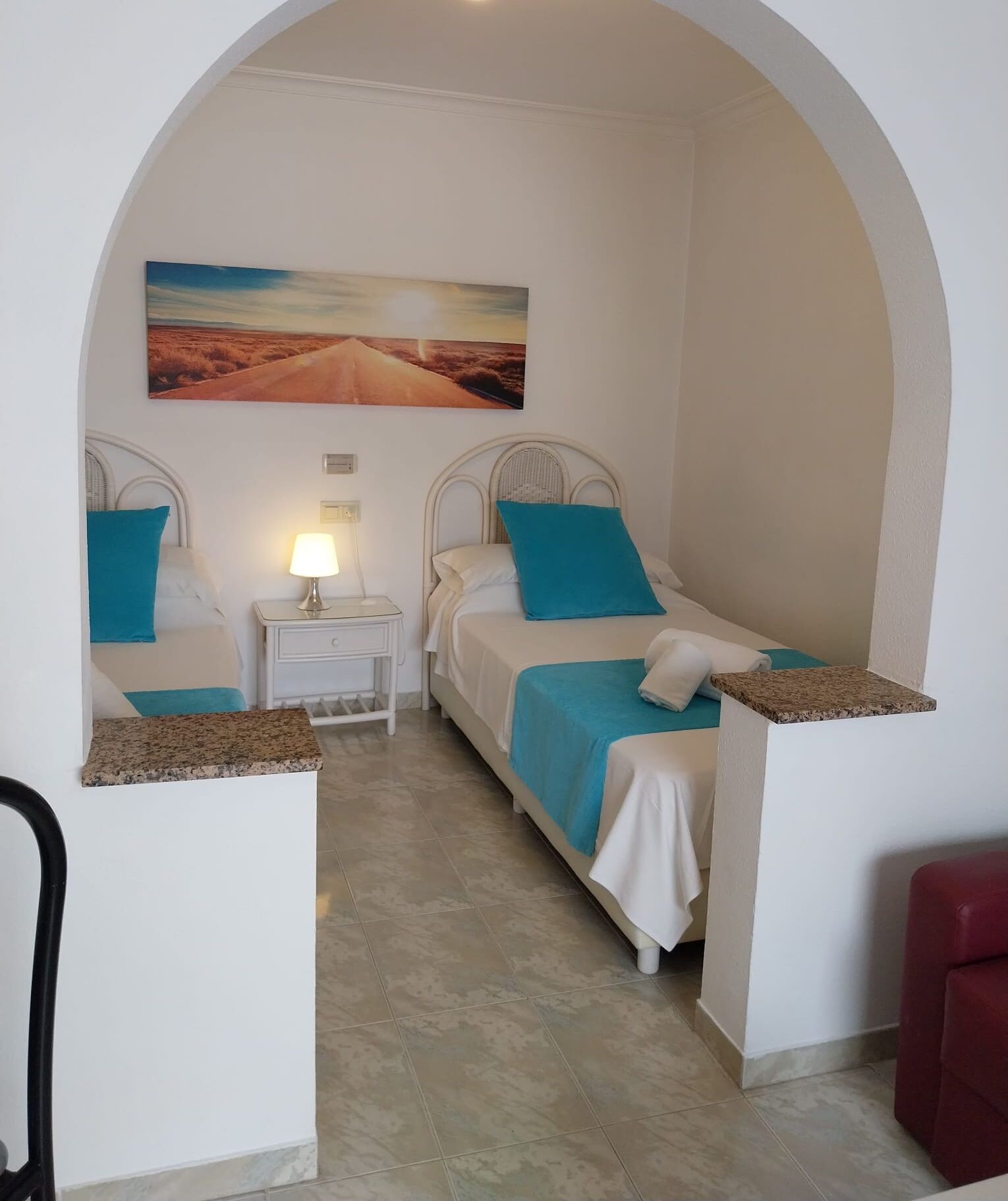 A room with two beds, a nightstand, a lamp, and a painting on the wall.