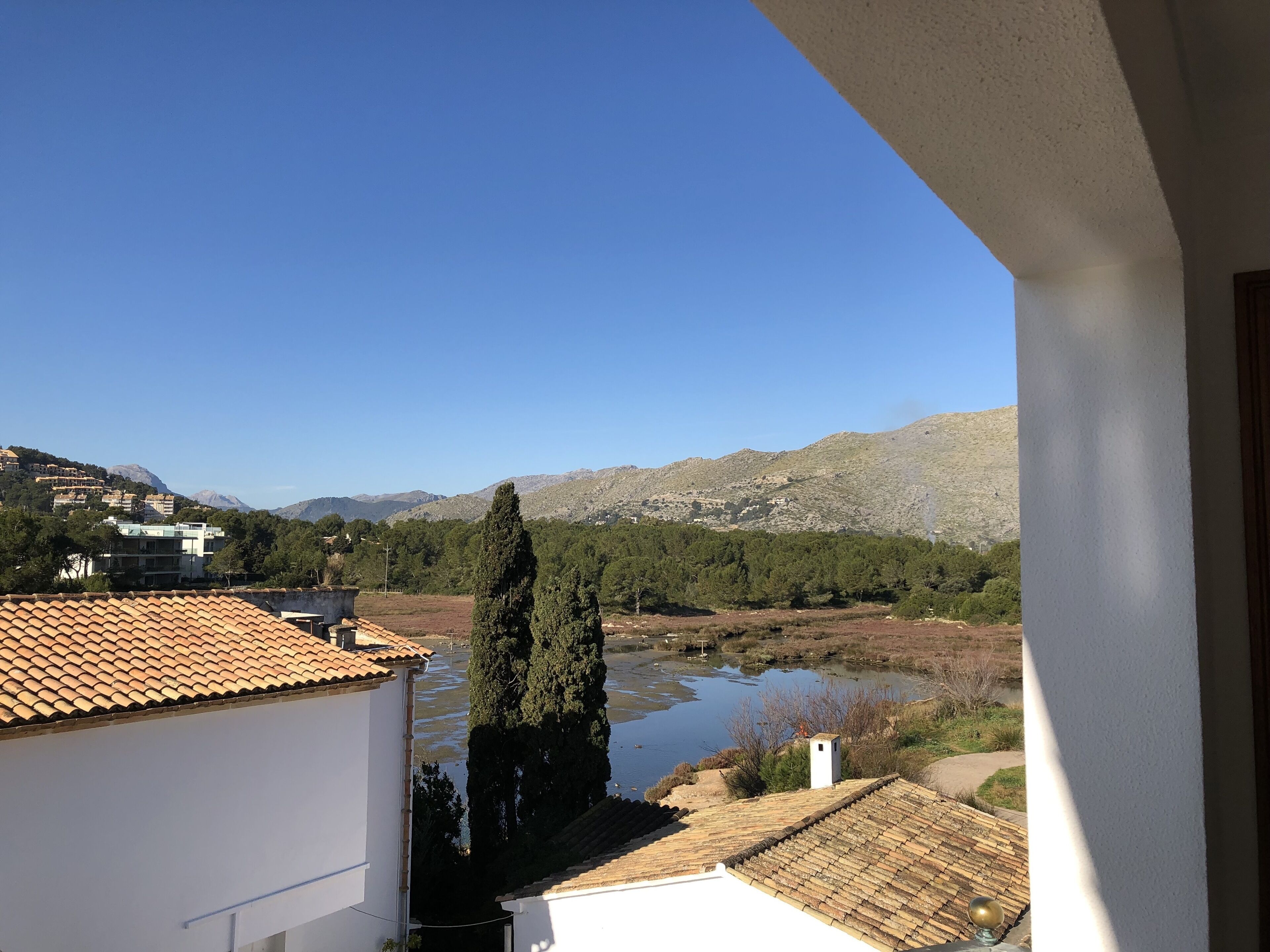 A view from a balcony overlooking a river, with buildings and mountains in the background.