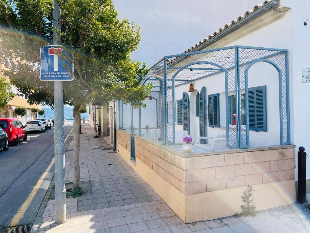 A building with a covered outdoor seating area, a street sign, parked cars, and a sidewalk.