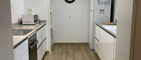 A compact kitchen with white cabinets, a microwave, a stove, and a refrigerator.