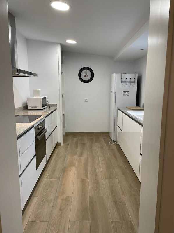 A compact kitchen with white cabinets, a microwave, a stove, and a refrigerator.