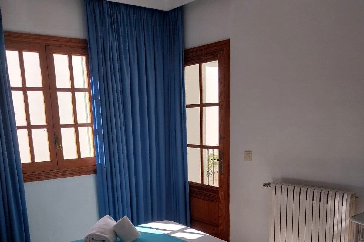 Habitación de hotel con dos camas, cortinas azules, ventanas de madera y un radiador.