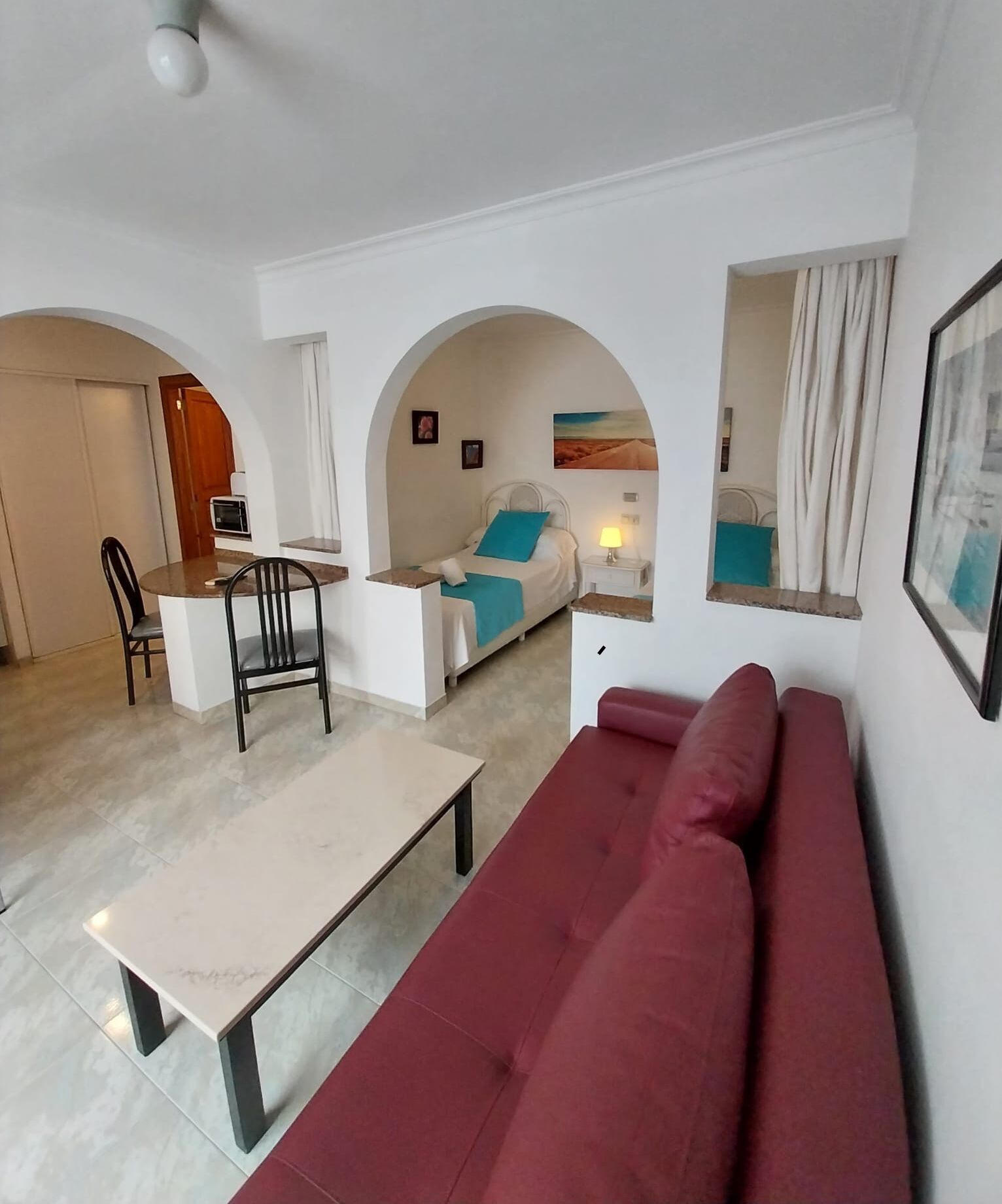A modern living room with a red sofa, a dining table with chairs, and a kitchen area visible through an archway.