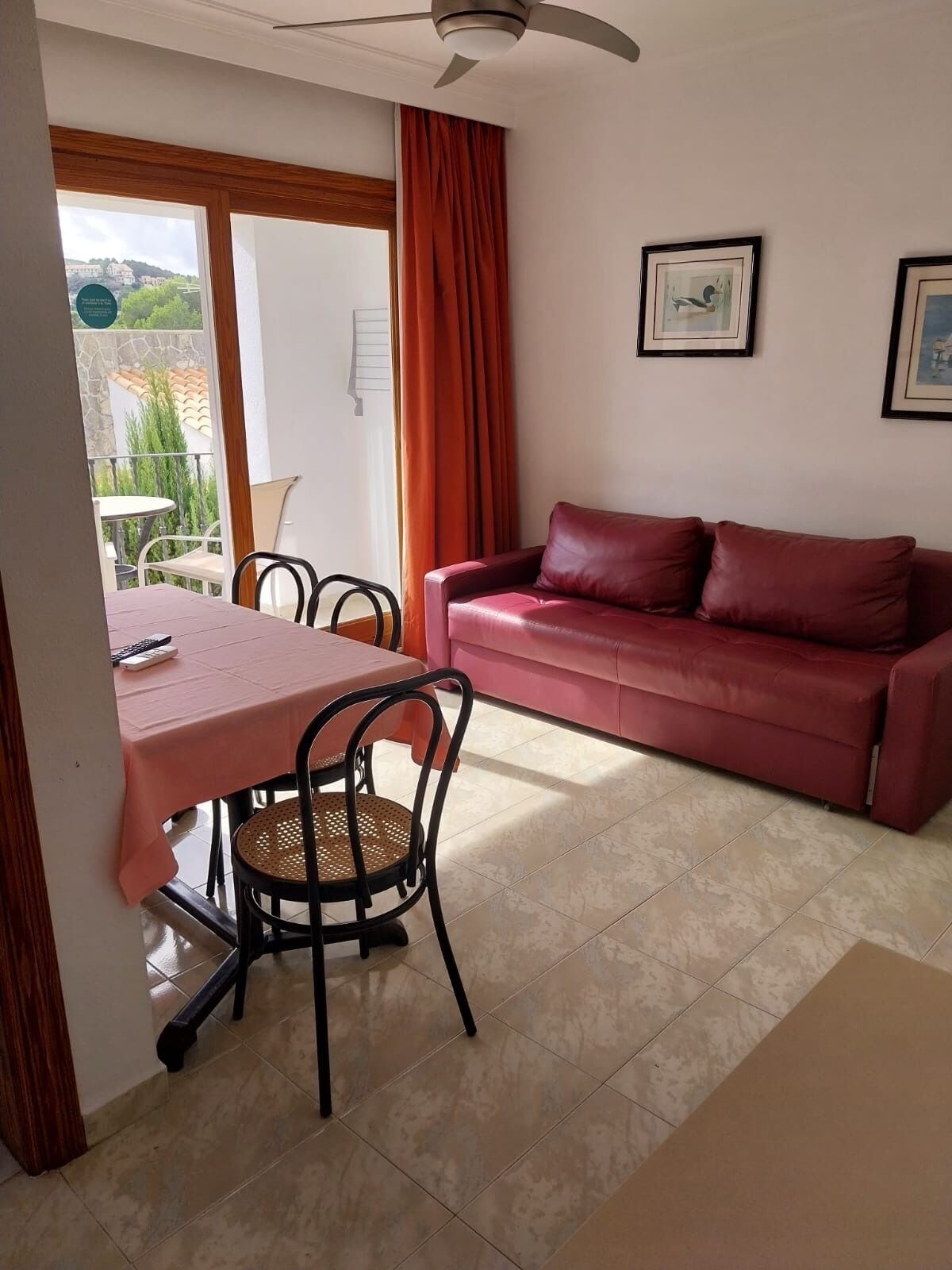 A room with a dining table, chairs, a red sofa, a ceiling fan, and a view of the outdoors.