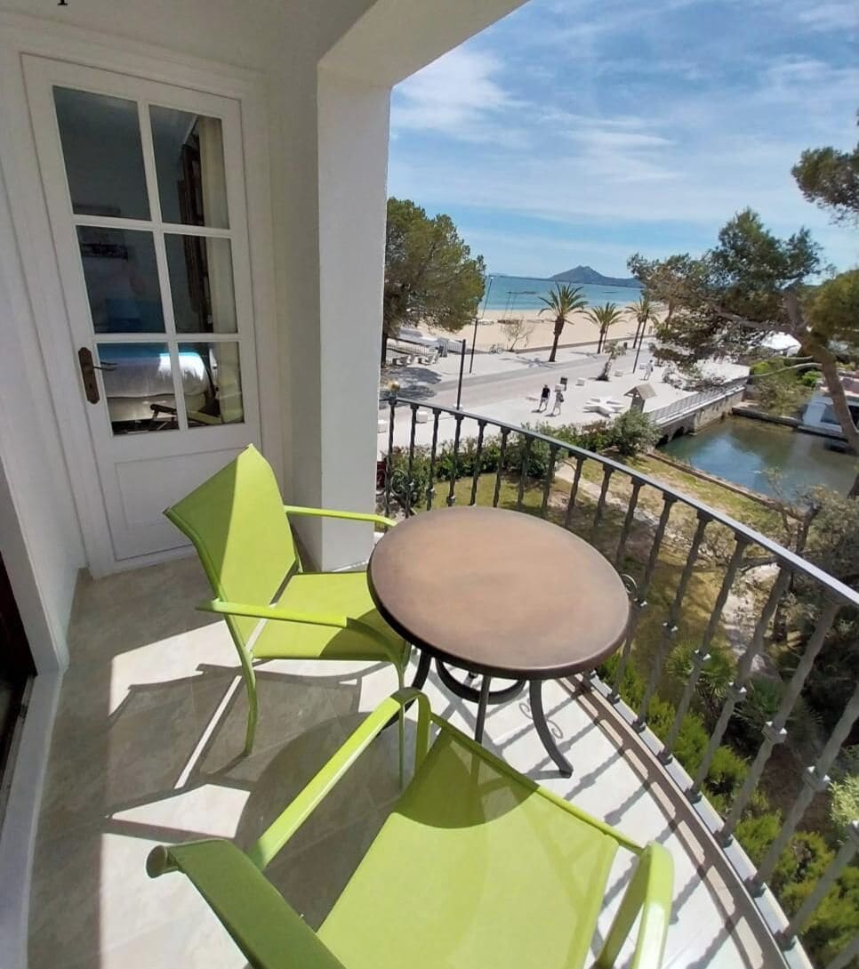 Een balkon met een tafel en stoelen, met uitzicht op een strand en een wateroppervlak.
