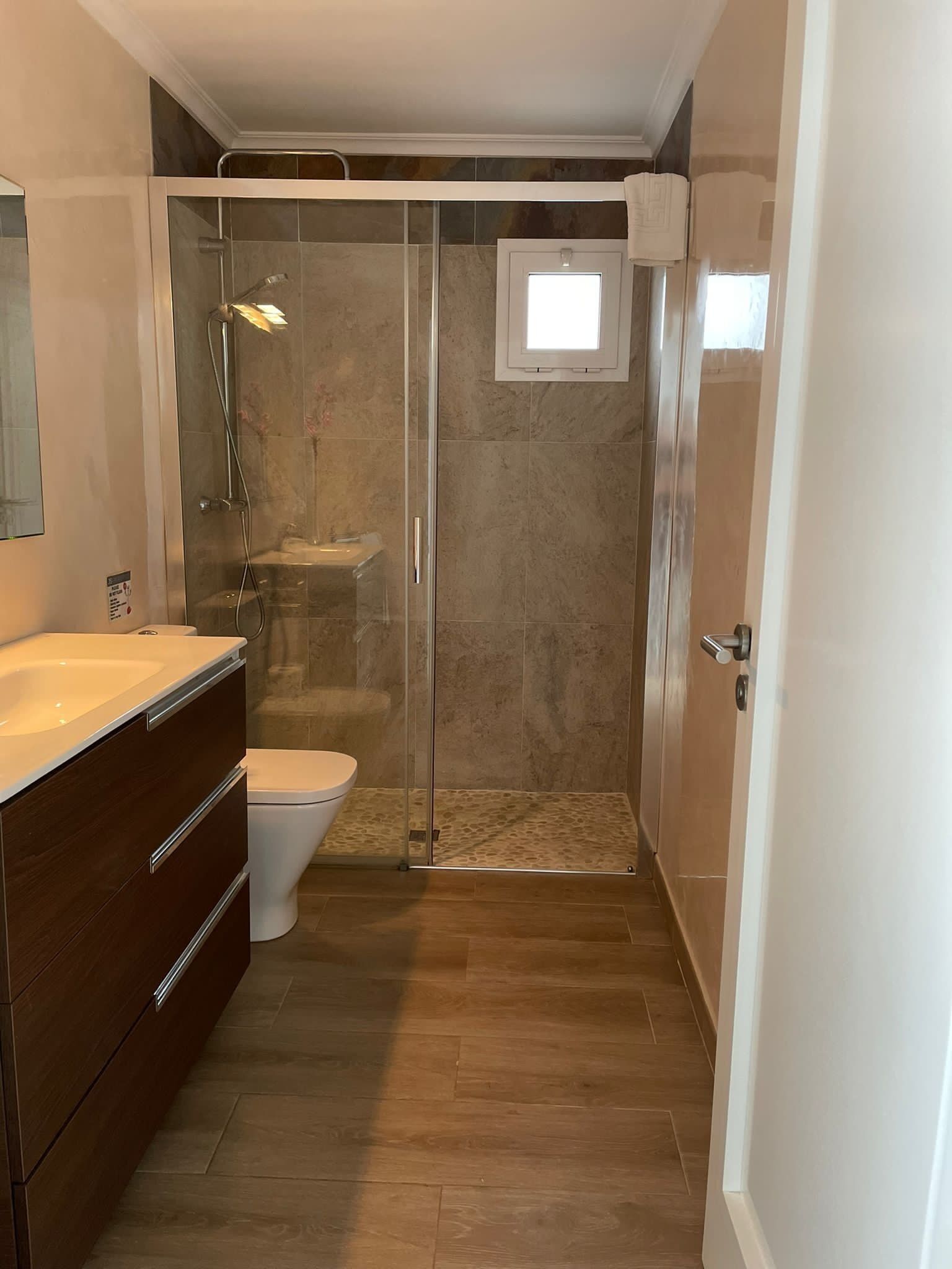 A bathroom with a glass-enclosed shower, a toilet, and a vanity with drawers.