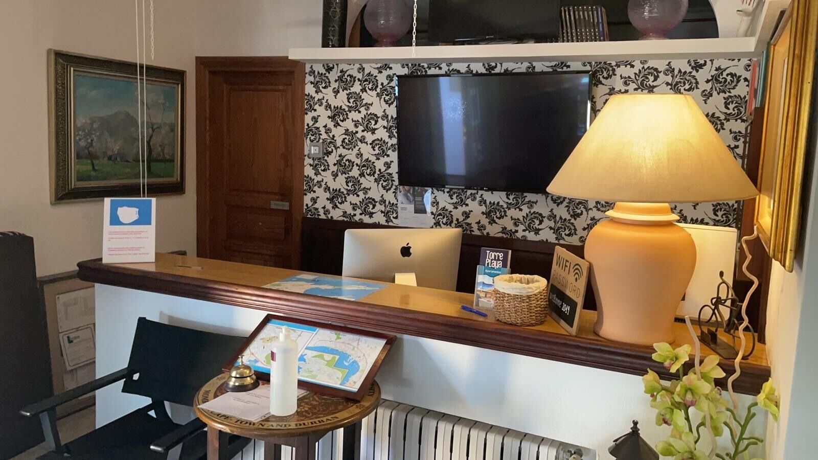 Una reception con un laptop, una mappa, un quadro incorniciato, una lampada e un segnale che indica la disponibilità del WiFi.