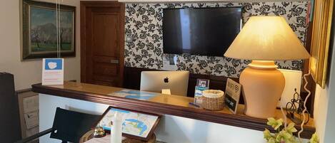 Una reception con un laptop, una mappa, un quadro incorniciato, una lampada e un segnale che indica la disponibilità del WiFi.
