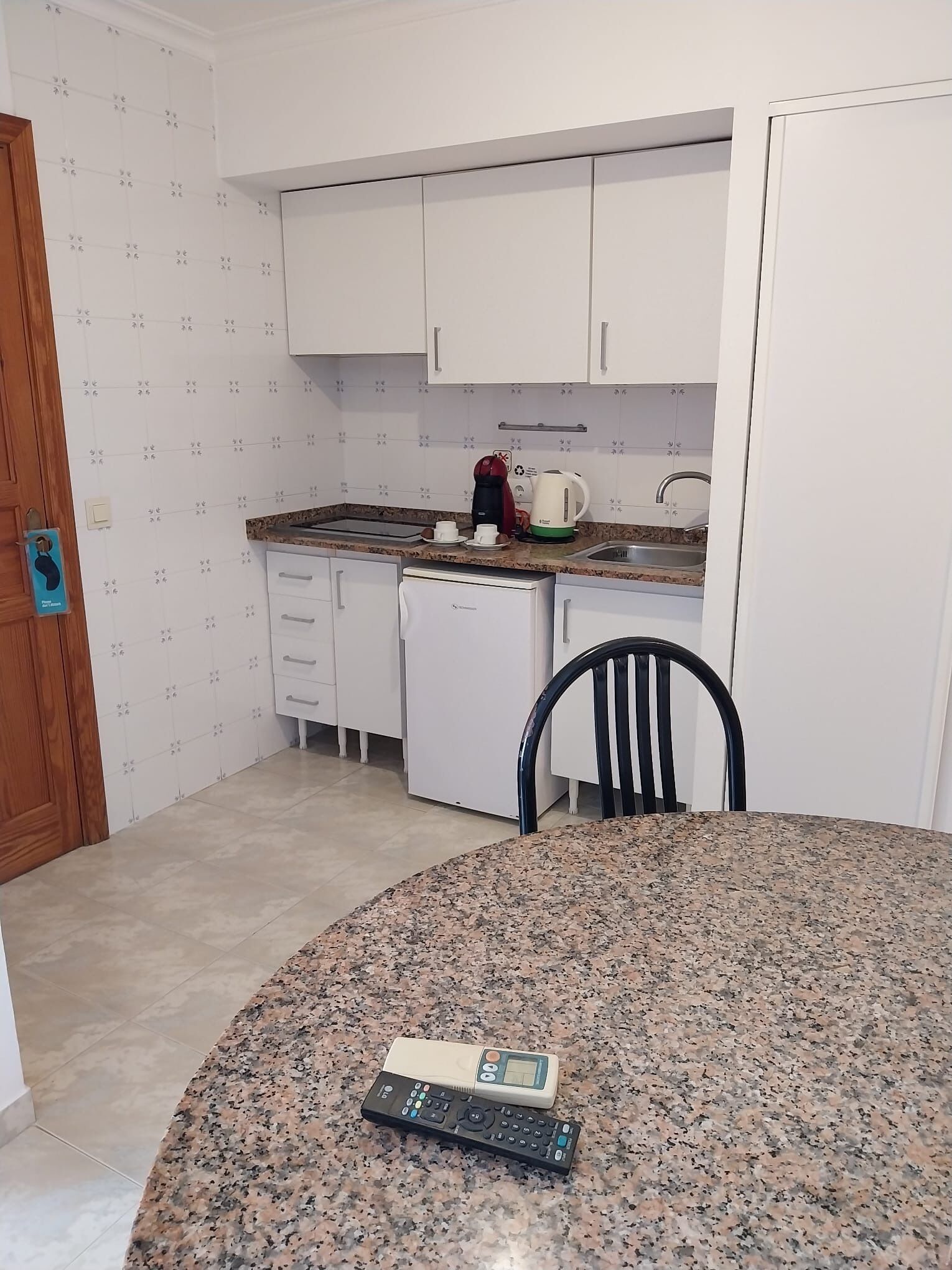 A compact kitchen with white cabinets, a granite countertop, a coffee maker, and a small dishwasher.