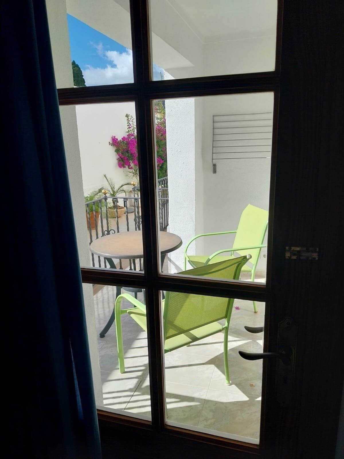 A view through a glass door to an outdoor patio area with a round table and two green chairs.