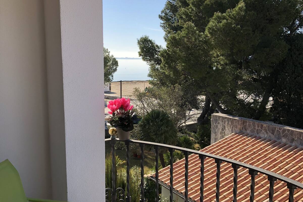 Un balcón con una mesa, una silla y vistas al mar y a los árboles.