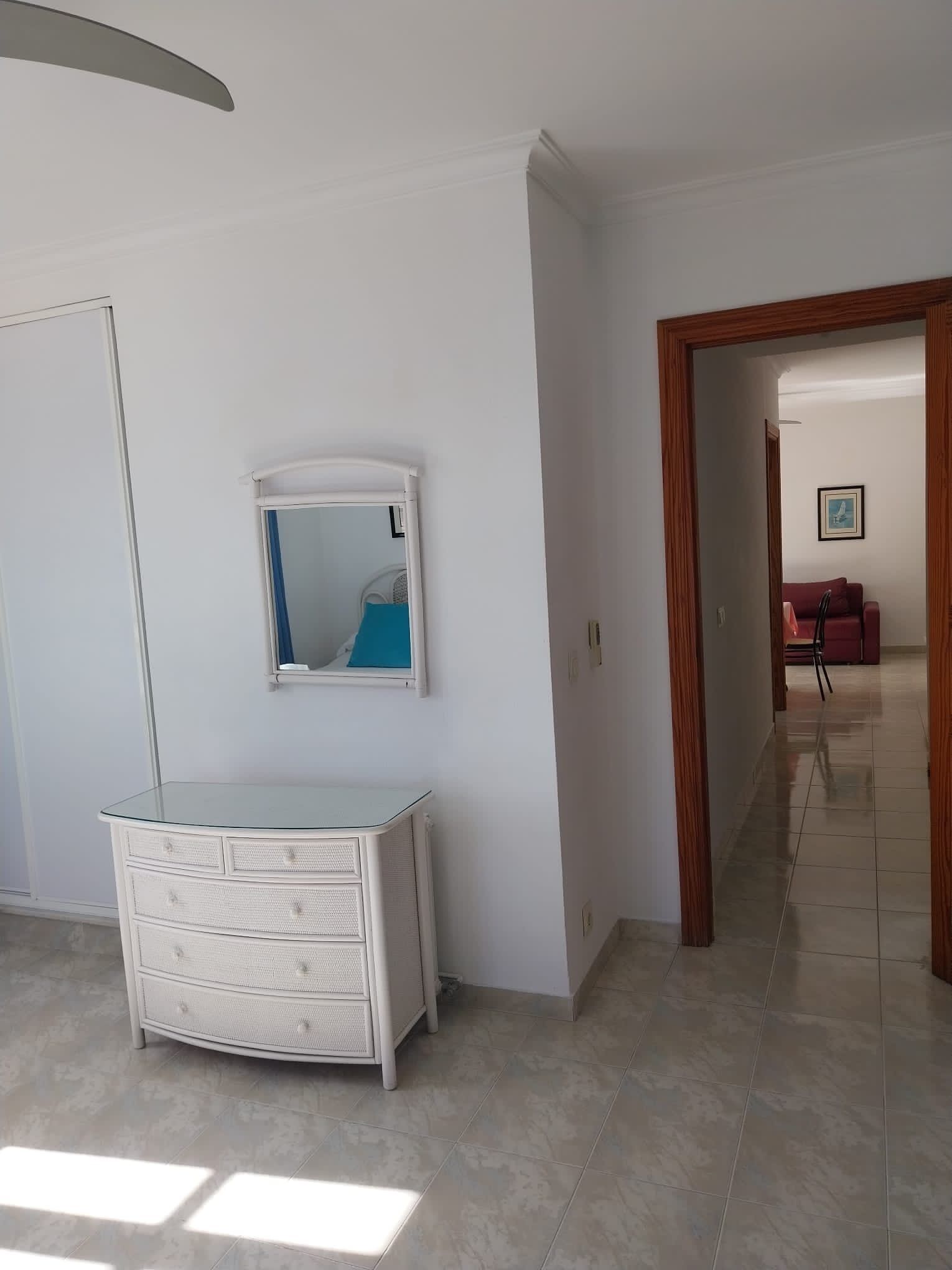 A room with a white dresser, a mirror, and a door leading to another room.