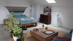 Ein Schlafzimmer mit einem Bett, einem Nachttisch, einer Kommode, einem Spiegel, Topfpflanzen und einem Deckenventilator.