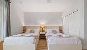 Une chambre d’hôtel avec deux lits, une table de chevet avec une lampe et une grande fenêtre avec des rideaux.