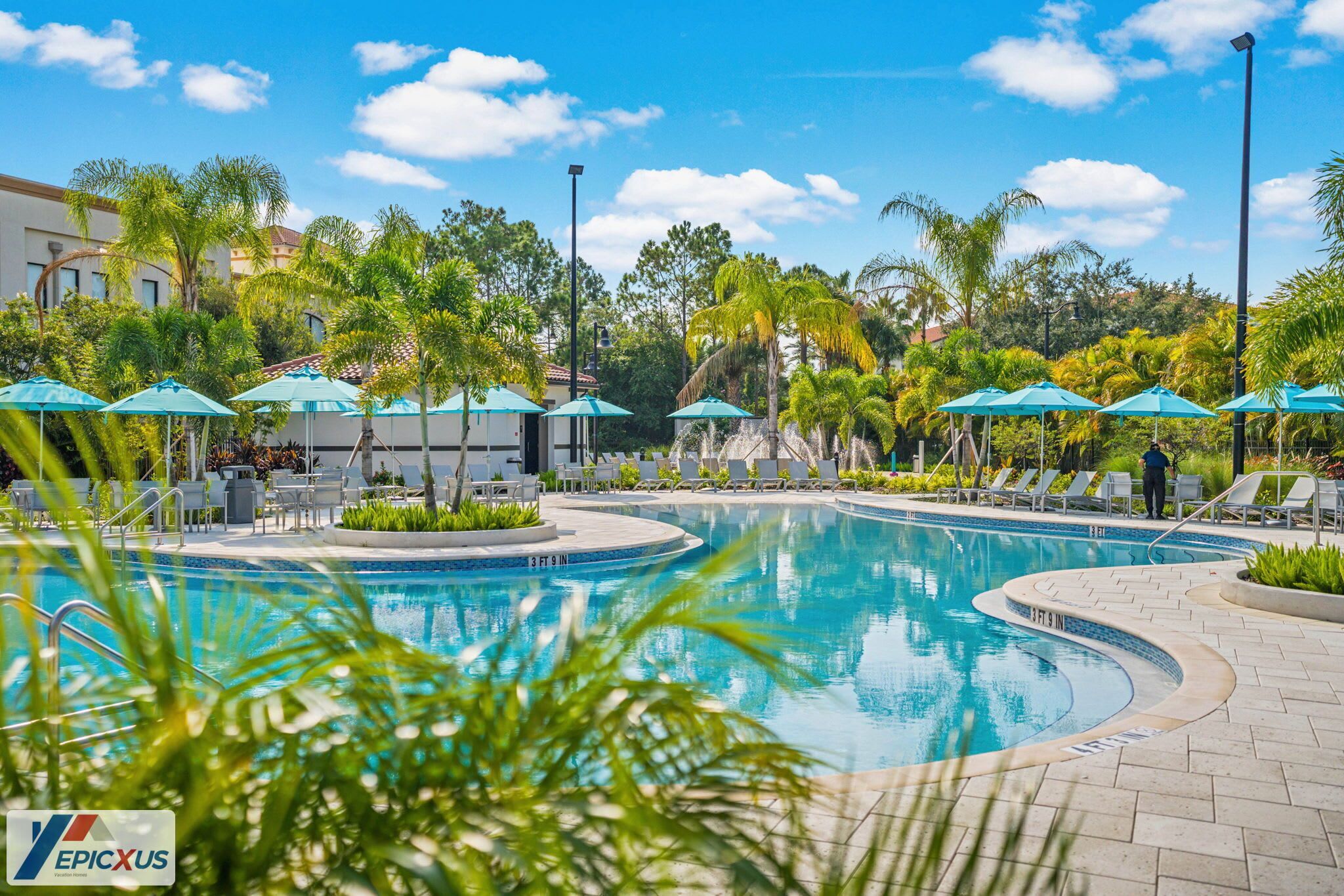 A swimming pool with lounge chairs and umbrellas, surrounded by palm trees and a clear sky.