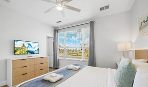 Una habitación de hotel con cama, televisión sobre una cómoda de madera, ventana con persianas y ventilador de techo.