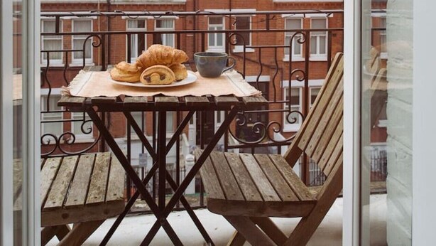 Un balcón con una mesa, una silla y un croissant, con vista a una hilera de edificios de ladrillo rojo.
