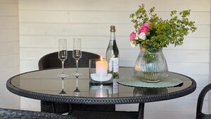 A round glass table with a bottle, two glasses, a candle, and a vase with flowers. - Ferienwohnung mit Weitläufigen, Parkähnlichen Garten, Pavillon und Bouleplatz (Bosau)