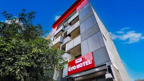A hotel building with a red and grey facade, balconies, and a clear blue sky. - Umen Hotel Sector 66 (Noida)