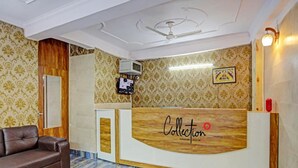 A reception area with a wooden reception desk, a brown leather sofa, patterned wallpaper, a ceiling fan, and a framed picture on the wall. - Umen Hotel Sector 66 (Noida)