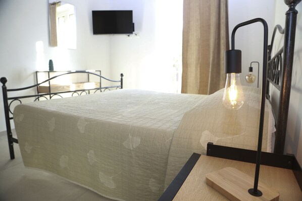 Una cama bien hecha con una colcha acolchada, una mesita de noche con lámpara y un televisor montado en la pared.