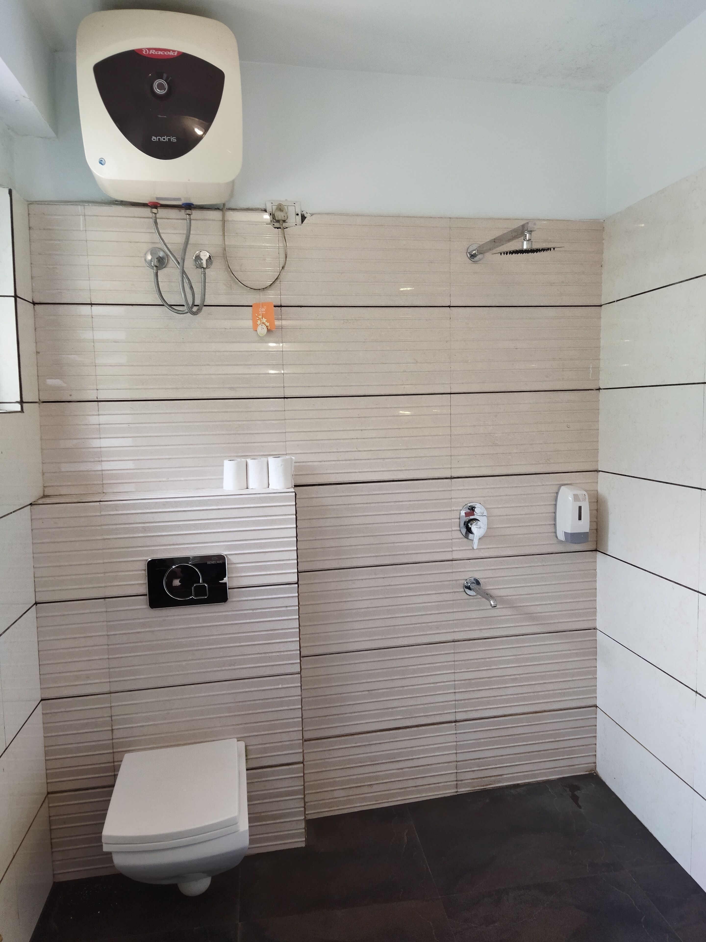 A bathroom with a toilet, a hand dryer, a towel dispenser, and a showerhead.