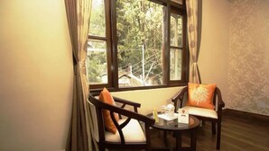 A cozy room with two wooden chairs, a small round table, and a window offering a view of a tree and a structure outside. - Dew Pond (Gangtok)