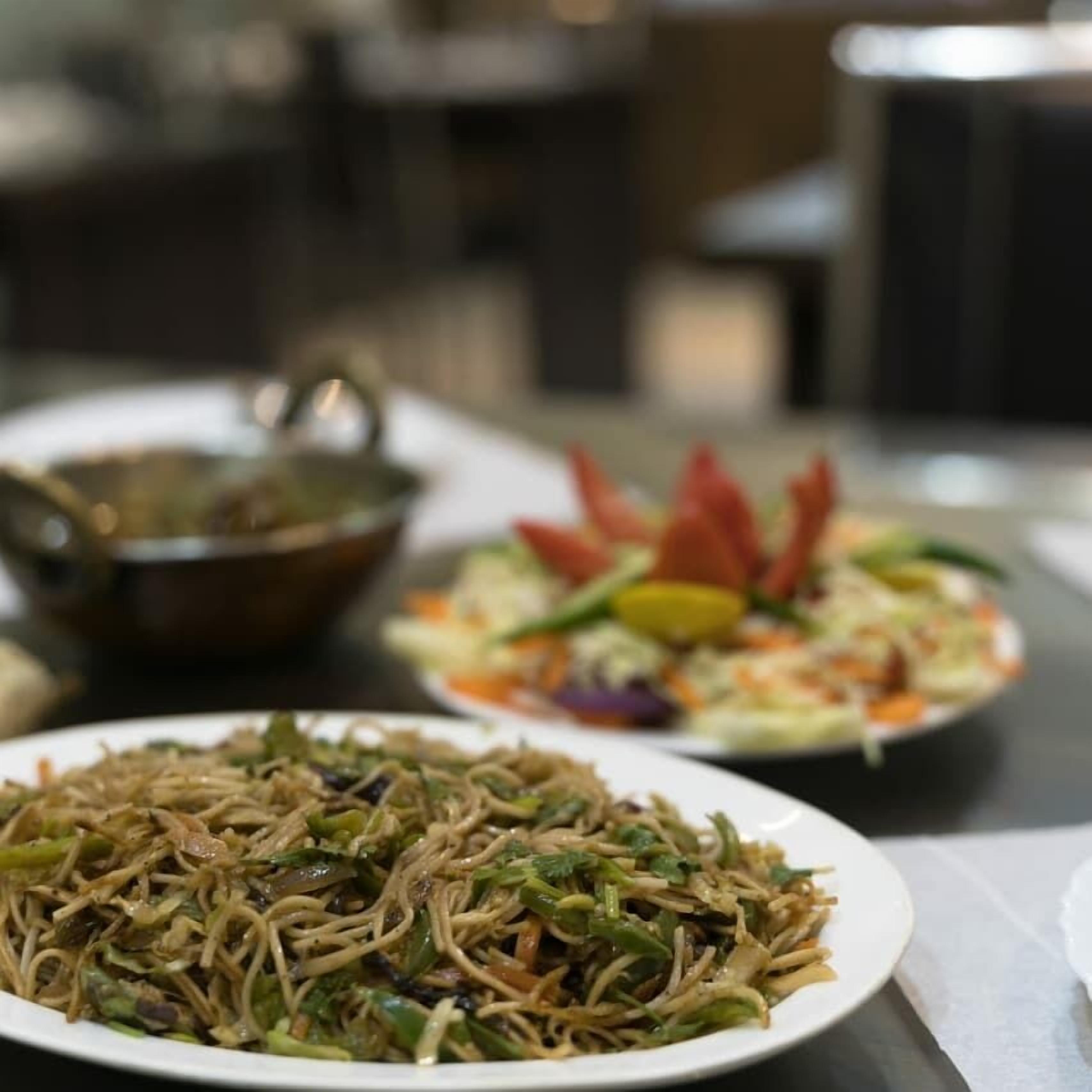 Una mesa con un plato de fideos, un tazón y una ensalada.