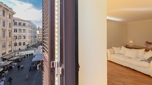 Ein Zimmer mit einem weißen Sofa, Holzboden und Blick auf eine belebte Straße mit Gebäuden und Menschen.