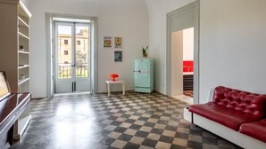 A spacious living room with a checkered floor, a red leather sofa, a teal refrigerator, and a white piano.