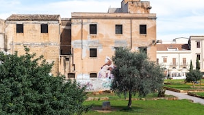 A historic building with a mural, surrounded by greenery and a clear sky.