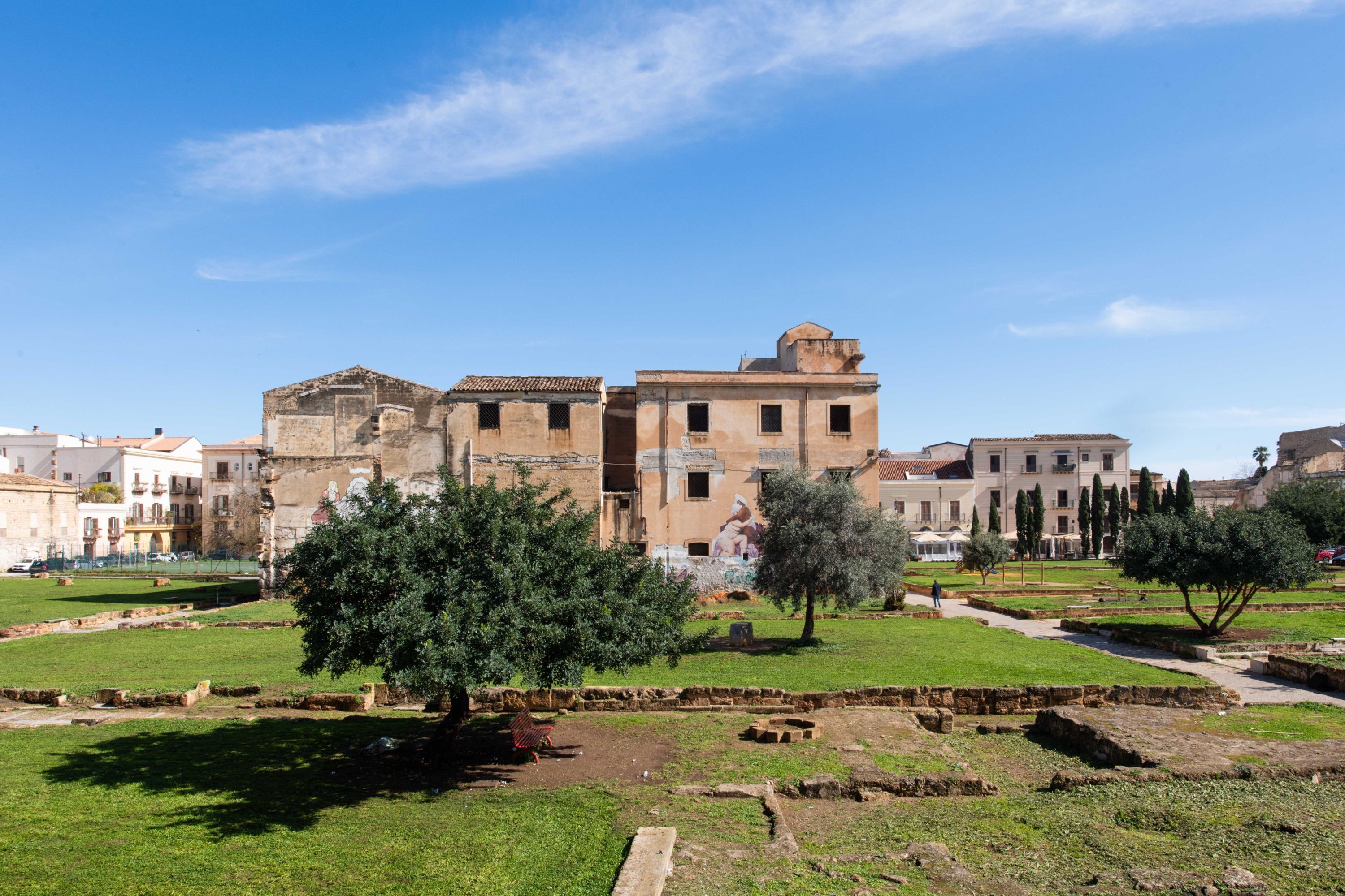 Ruinas antiguas con un edificio central, rodeado de vegetación y otras estructuras históricas.