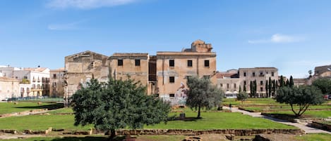 Eine alte Ruine mit einem zentralen Gebäude, umgeben von Grünflächen und weiteren historischen Bauwerken.
