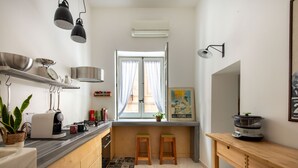 A compact kitchen with a built-in stove, a coffee machine, and a sink. There are two stools and a wooden table.