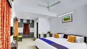 A hotel room with a large bed, a desk, a chair, a ceiling fan, and a picture on the wall. - Yahweh Suites (Bengaluru)