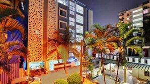 A modern hotel with a central courtyard, palm trees, and a car parked outside. - Yahweh Suites (Bengaluru)