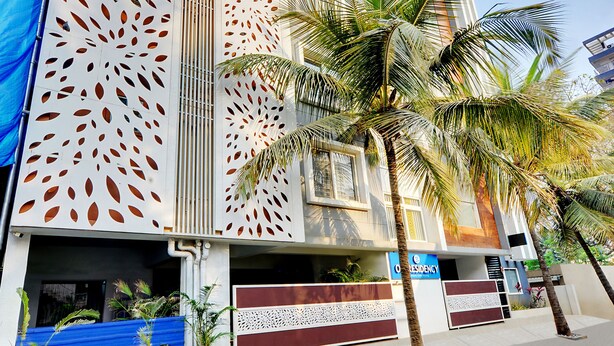 A modern building with a unique perforated facade, palm trees, and a clear blue sky. - Yahweh Suites (Bengaluru)